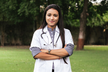 Portrait of confident Indian doctor wear white coat standing at outdoors with arms crossed on chest. Professional occupation person during covid-19, concept of medical service In India