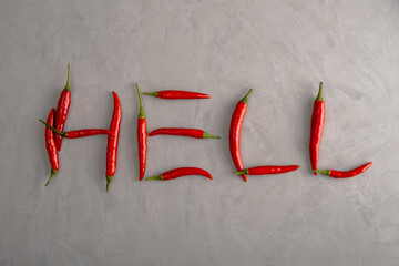 Word Hell is lined with pods of ripe red hot chili peppers on gray surface with a stucco texture. Selective focus.