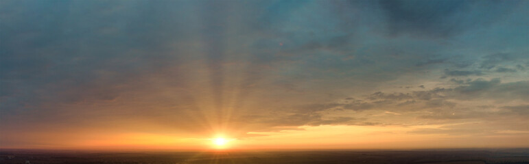 Sunrise with sunbeams from behind the clouds. Panorama of the morning sky with colorful clouds in the sky.