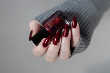 Female hand with long nails and a dark red manicure holds a bottle of nail polish