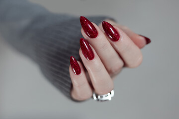 Female hand with long nails and a dark red manicure holds a bottle of nail polish