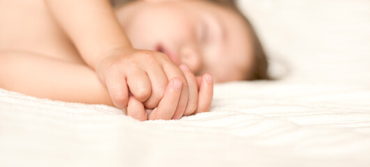 A pretty baby sleeps comfortably on the bed. Close-up hands of a beautiful sleeping baby