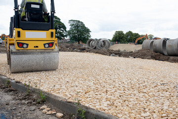 Road roller compacting stone during new road construction in preparation for tarmac, on housing...