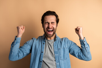 Overjoyed handsome man in denim casual shirt expressing winning gesture with raised fists