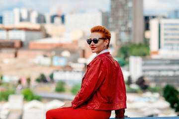 Obraz premium a red-hair woman in a red trousers and coat sitting in front of the city on an summer day