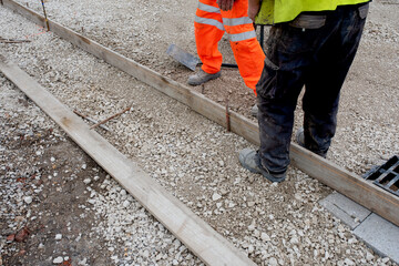 Groundworker in orange safety hi vis trousers fixing a timber along string line with steel pin to...