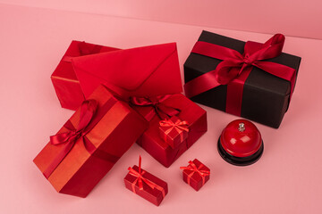 high angle view of red wrapped gift boxes and envelope near metallic bell on pink.