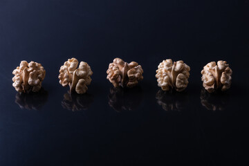 A row of beautiful tasty whole walnut kernels on a black glossy background. The concept of the usefulness of walnuts. Copy space view