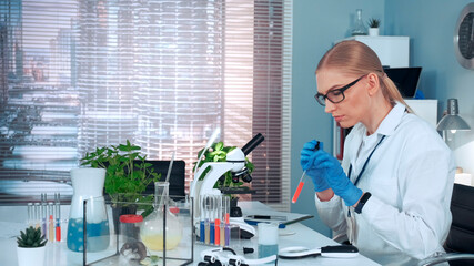 In modern research laboratory: female scientist using pipette to drop sample on slide and looking...