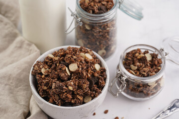Fototapeta na wymiar Breakfast muesli cereal with chocolate chips and nuts in several jars and bowl, bottle of milk, white surface