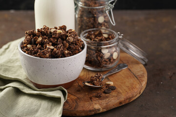 Fototapeta na wymiar Breakfast muesli cereal with chocolate chips and nuts in several jars and bowl, bottle of milk, brown wooden surface