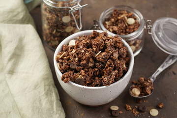 Breakfast muesli cereal with chocolate chips and nuts in several jars and bowl, bottle of milk,...