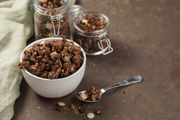 Breakfast muesli cereal with chocolate chips and nuts in several jars and bowl, bottle of milk, brown wooden surface