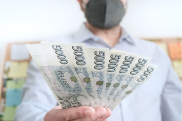 Finance during coronavirus in Czechia concept. Czech Koruna CZK 5000 banknotes. Man in a protective medical face mask respirator holds krona cash.