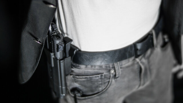 Man moving jacket to reveal a holstered firearm. Open carry and second amendment concept
