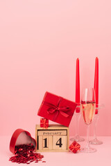 red gift boxes on calendar with 14 february lettering near champagne in glass, candles and confetti on pink.