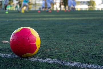 Colored ball on the white stripe of an artificial turf soccer training field. Blur of a group of...
