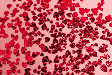 top view of shiny red confetti hearts on pink.