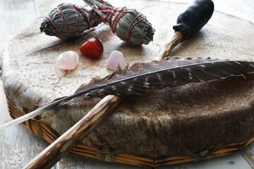 A side view image of a hand made leather meditation drum with white sage smudge sticks and sacred feather. 