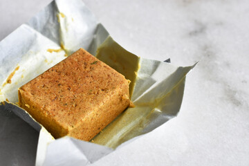 A close up image of a chicken bouillon cube in a silver wrapper. 