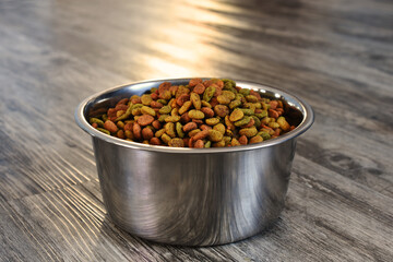 A low angle image of a bowl of cat food on a brown wooden floor. 