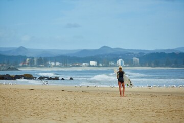 Fototapeta na wymiar A woman walking on the beach with her surfboard 