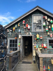 Vertical image of a wooden lobster shack covered in buoys and surrounded by lobster traps in a...