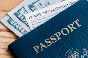 One Covid-19 Coronavirus vaccination card inside a blue American passport with some one hundred dollar bills cash requirement mandate law