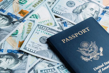 One blue American passport laying on a pile of American one hundred dollar bills