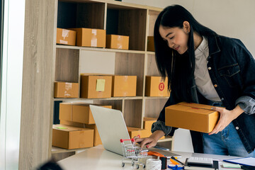 Small business, SME start-up, owner of Asian female entrepreneurs working with boxes and use a smartphone or laptop Receive and check online orders to prepare product boxes. Sell online sales ideas.