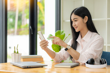 Beautiful Asian woman wearing headphones to listen to programs with the laptop to develop digital online courses. social distancing at home develop skills in the classroom to the career path