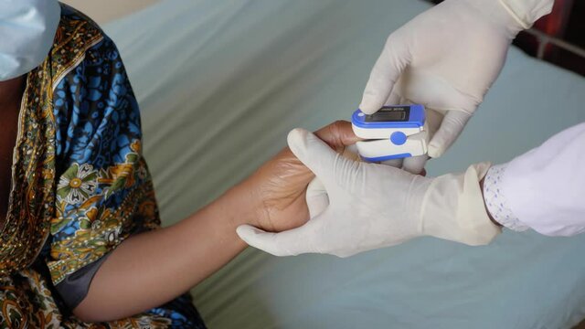Close up shot of an African male doctor checking a woman's blood oxygen levels with a pulse oximeter.