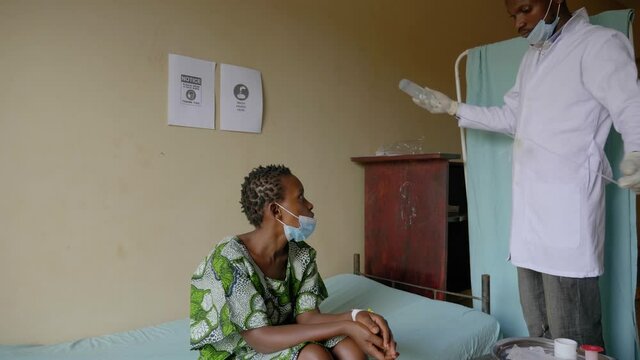 Wide shot African male doctor prepares an IV drip for a sick African woman in a rural clinic.