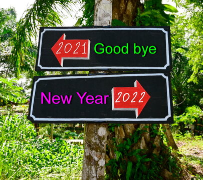 Wooden signs are painted in black with red arrows in opposite corners. with green text "2021 Good bye" and pink text "2022 New Year". Alternative concept between passing old year and upcoming new year
