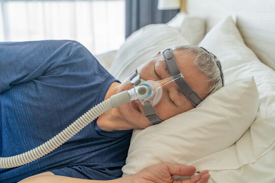 Middle age man wearing CPAP mask and headgear to help with his sleep apnea while sleeping in his bed