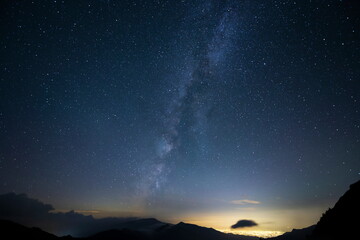 山の向こうの街明かりの上に輝く天の川