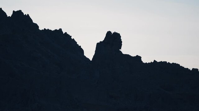 An outlandish landscape of the Varanger coast. The silhouette of the black jagged rocks against the pale grayish sky.