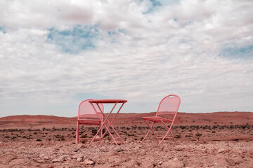 Two pink chairs and one table stand in the Namib desert against the backdrop of a cloudy sky