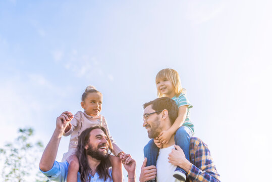 Gay Male Couple Holding Their Young Children On Their Shoulders