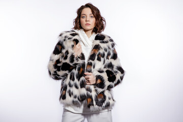 High fashion photo of a beautiful elegant young woman in a pretty leopard print fur coat, trousers, pants, black sneakers posing over white background. Make up, hairstyle. Slim figure. Studio shot