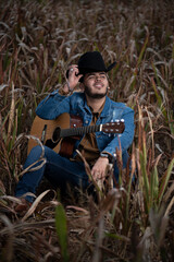 JOVEN MEXICANO CANTANDO CON SU GUITARRA USA SOMBRERO Y TIENE BARBA