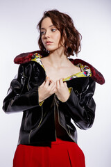 High fashion photo of a beautiful elegant young woman in a pretty black leather jacket, red trousers, pants posing over white background. Make up, hairstyle. Slim figure. Studio shot