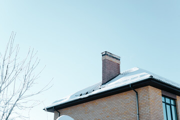 Snow-covered roof of country house with chimney on winter sunny day outside