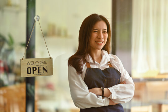 Photo of young restaurant owner standing with crossed arms over the restaurant glass doors as a background.