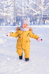 Fototapeta na wymiar A happy baby in winter clothes enjoys the snow while walking in a winter park