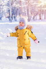 Fototapeta na wymiar Toddler 12-17 months old in yellow winter clothes rejoices in the fallen snow while walking in the winter park