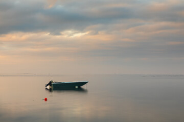 Barca di pescatori con motore ormeggiata al mare all' alba.  Cielo con nuvole colorate di rosa.