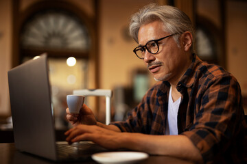 Businessman working on laptop in cafe. Handsome senior man enjoying in fresh coffee..