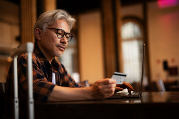 Businessman working on laptop in cafe. Handsome senior man enjoying in fresh coffee..