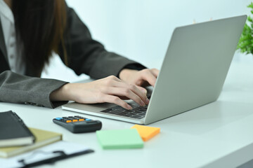 Cropped image of a young office woman hand typing on a computer laptop keyboard at the modern working desk surrounded by various office equipment.